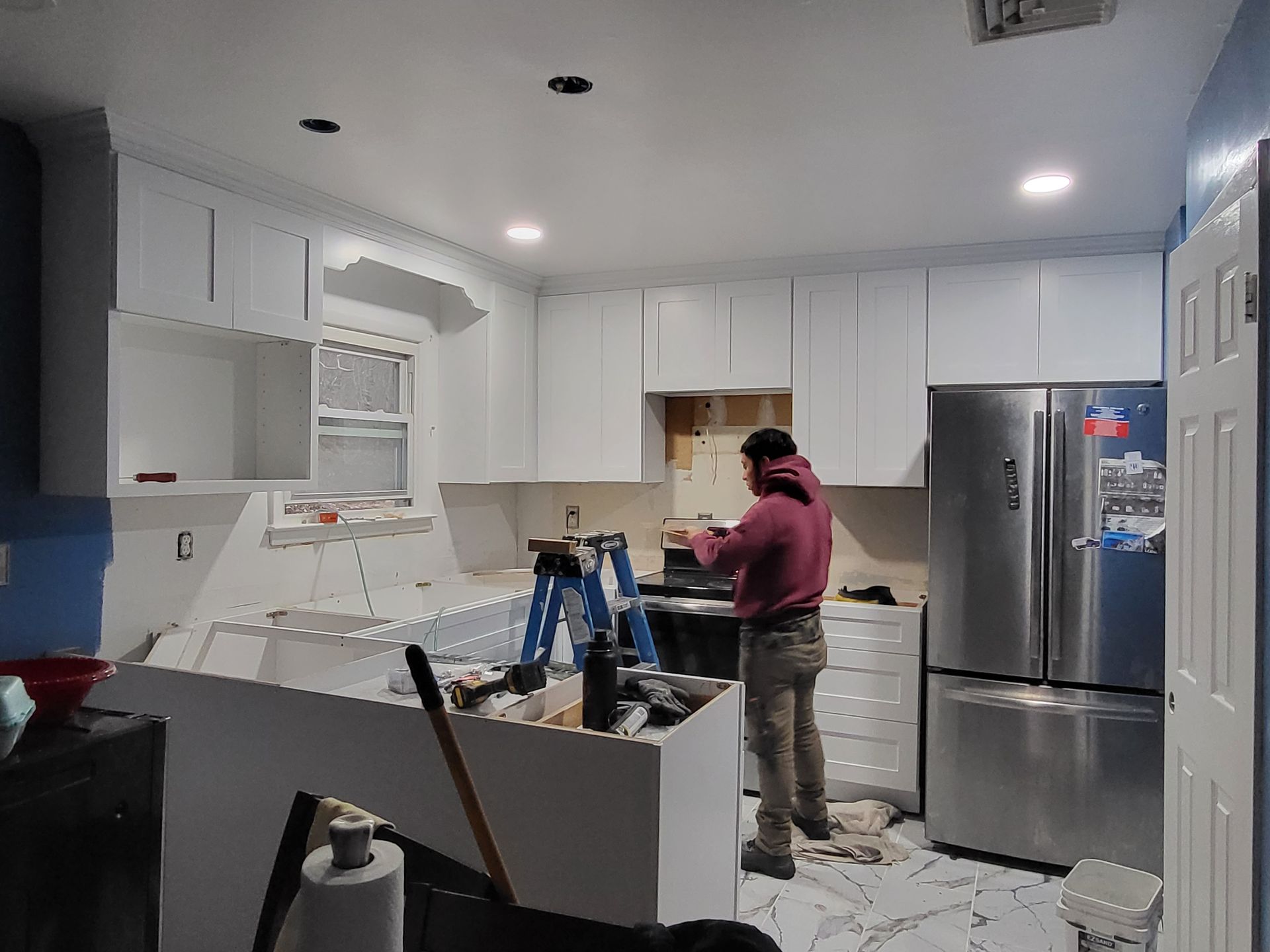a man is working in a kitchen with white cabinets and a stainless steel refrigerator