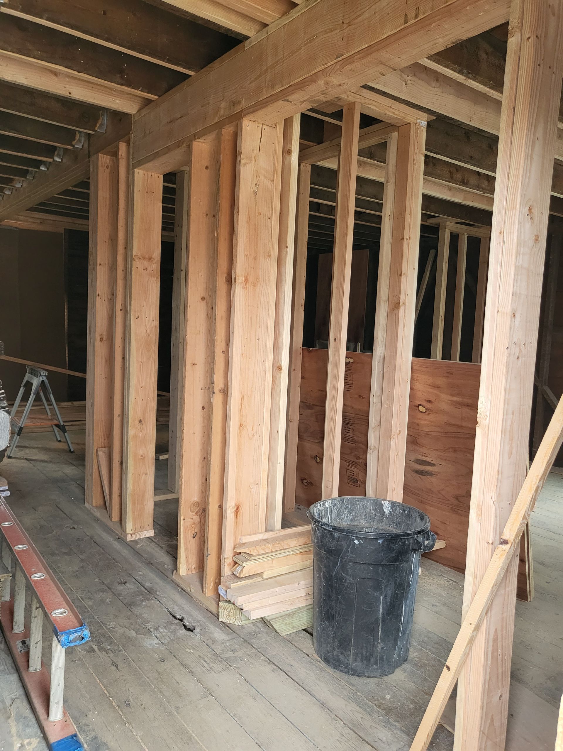 a black trash can is sitting in the middle of a wooden room under construction