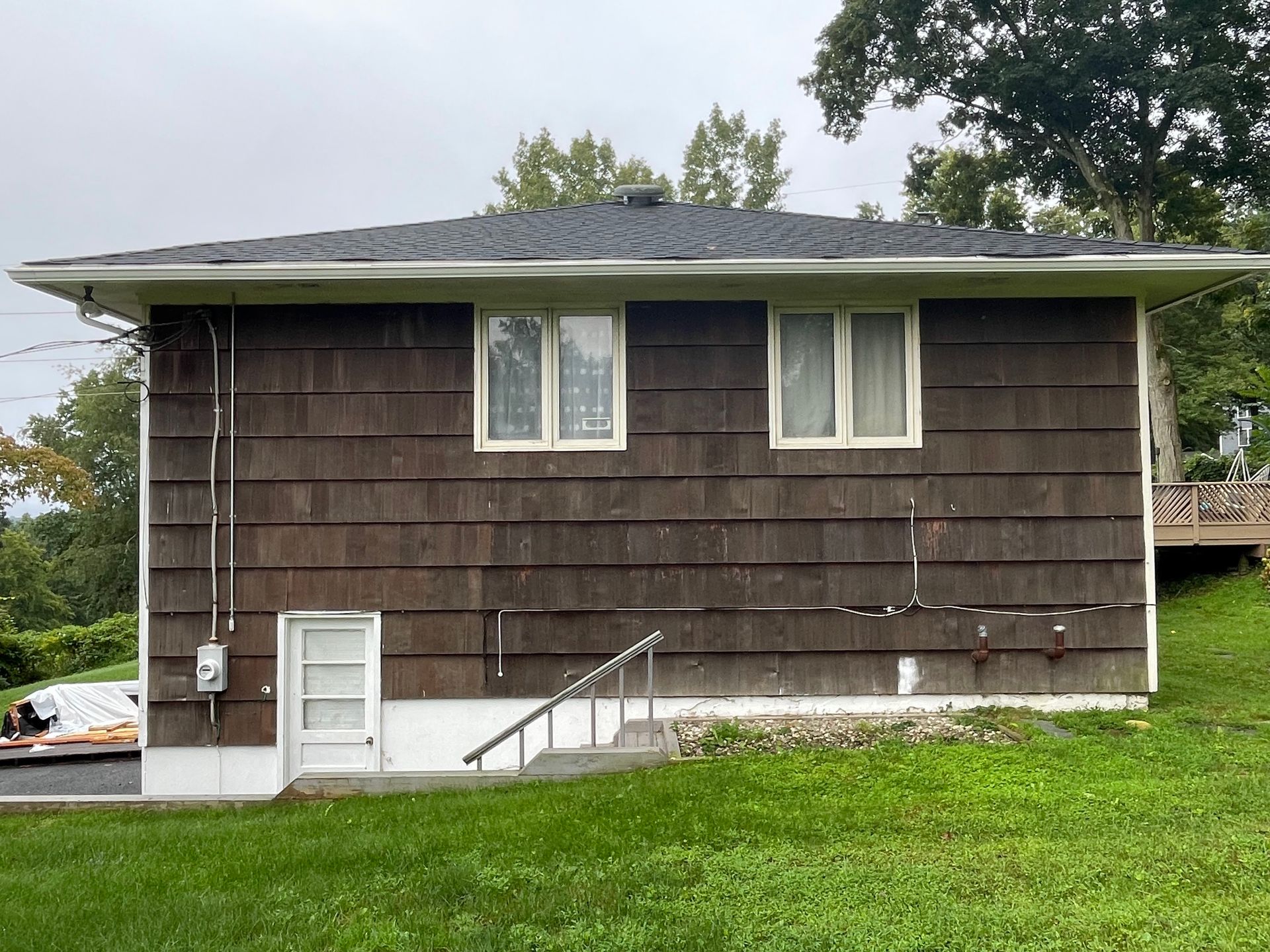 a small brown house with a black roof is sitting on top of a grassy hill