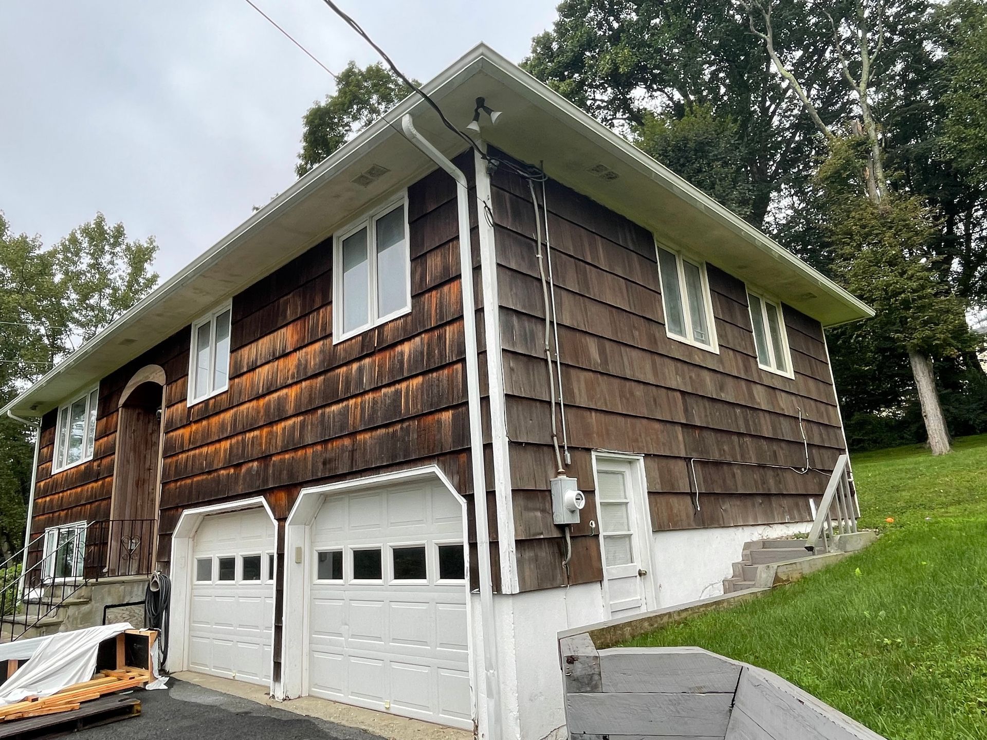 a brown house with a white garage door is sitting on top of a grassy hill