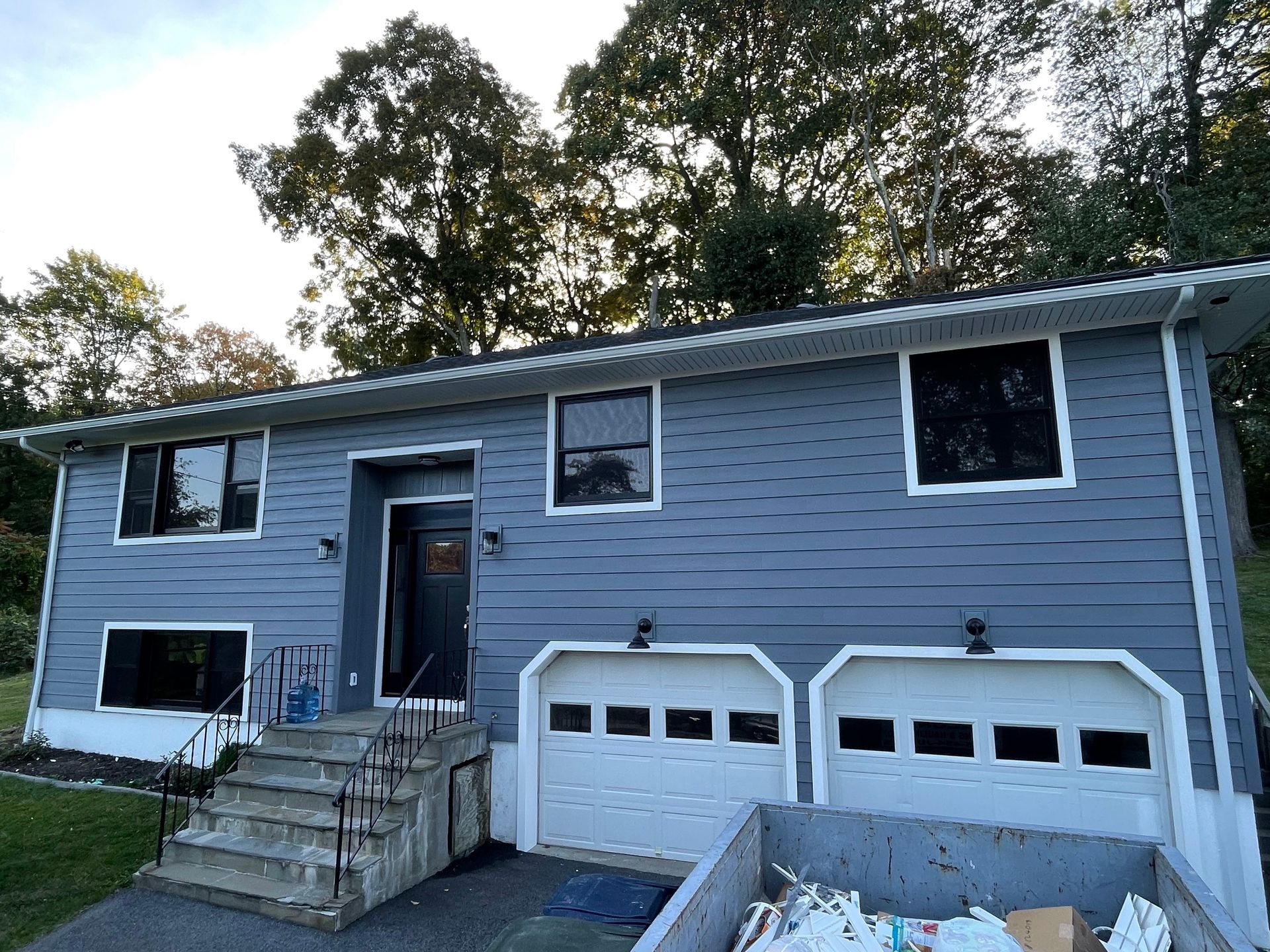 a blue house with two garage doors and a dumpster in front of it