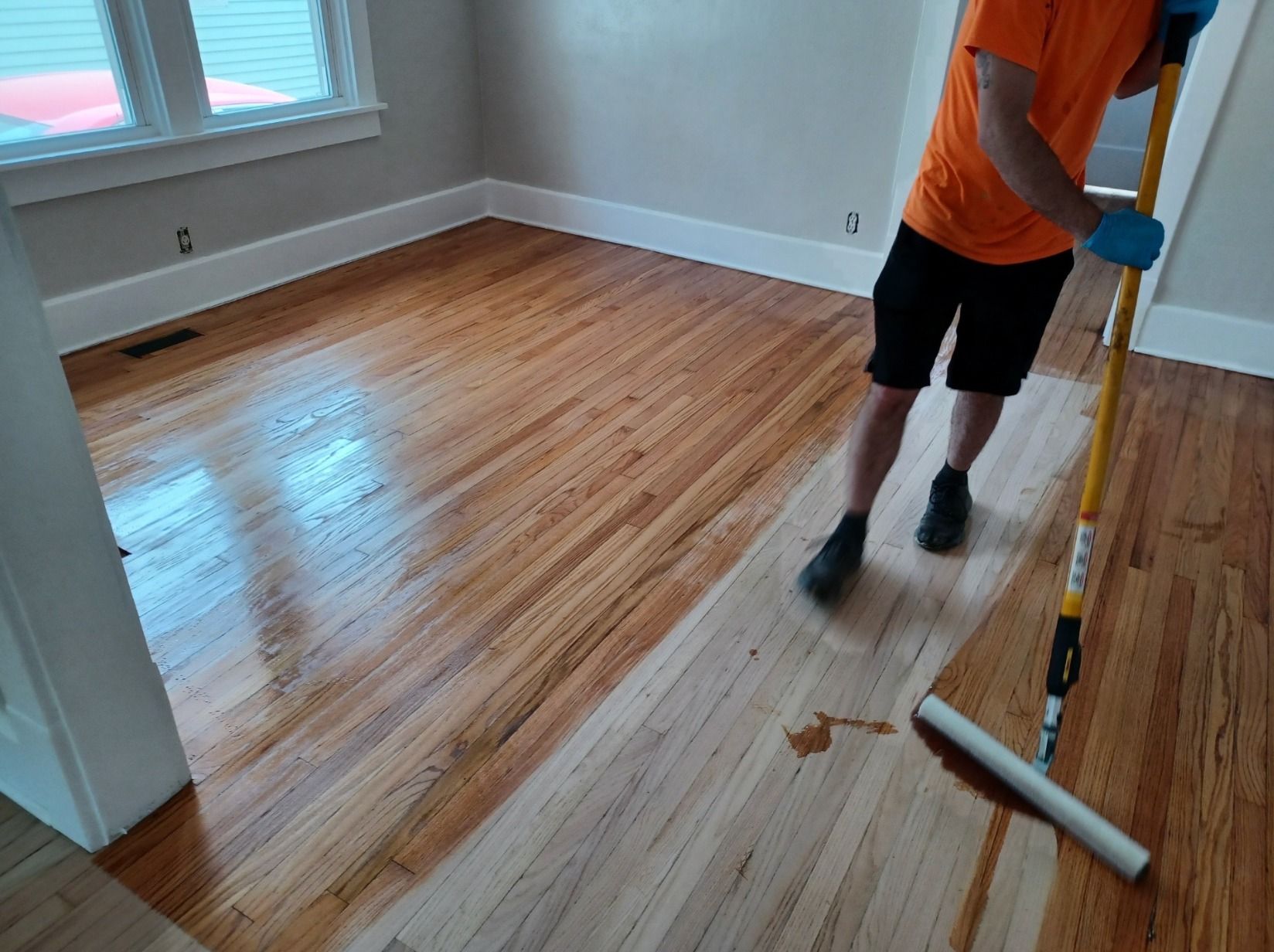A man is painting a wooden floor with a roller.