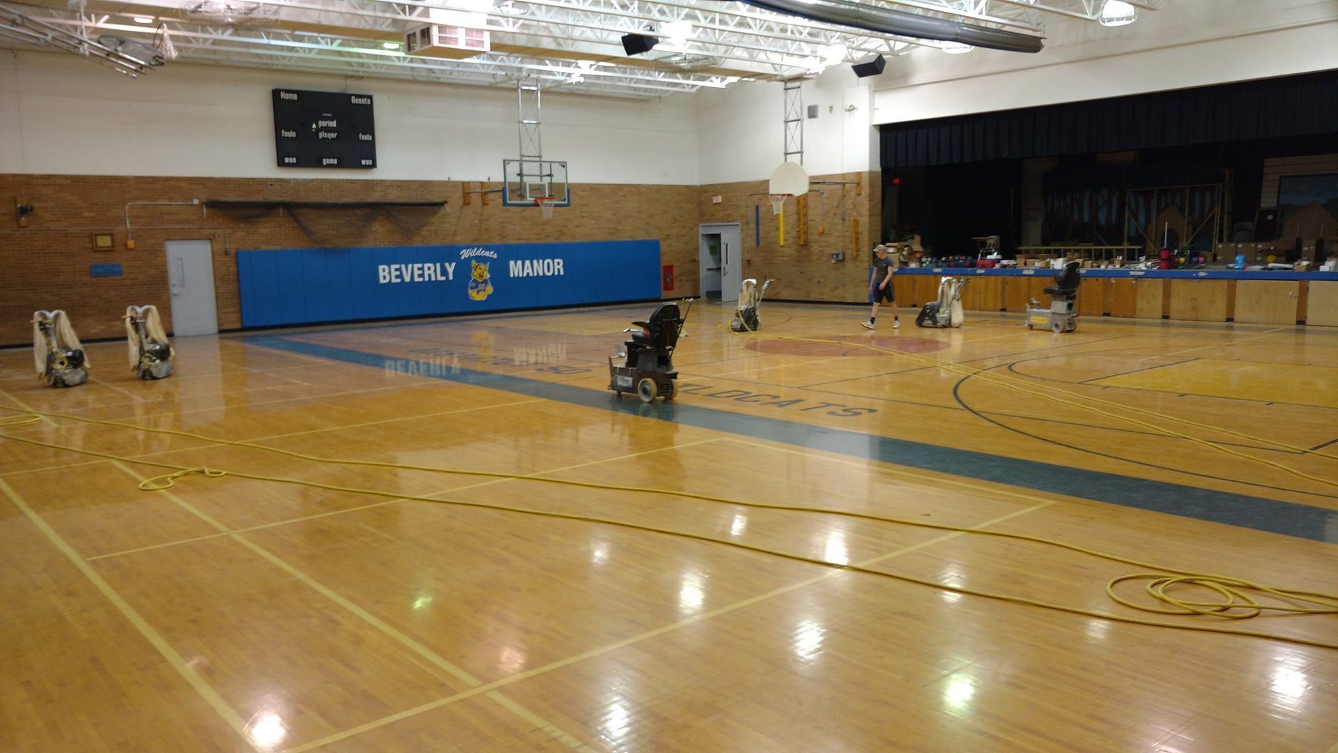 A person in a wheelchair is sitting on a wooden floor in a gym.