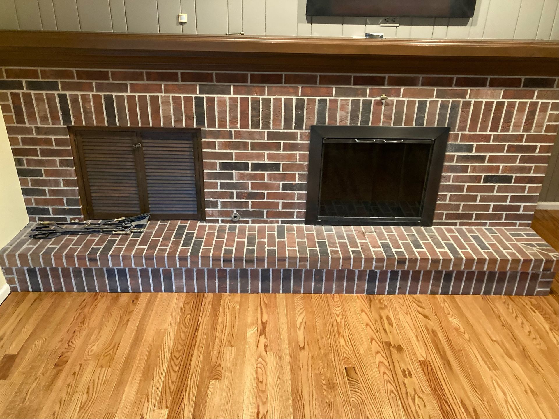 A brick fireplace in a living room with hardwood floors
