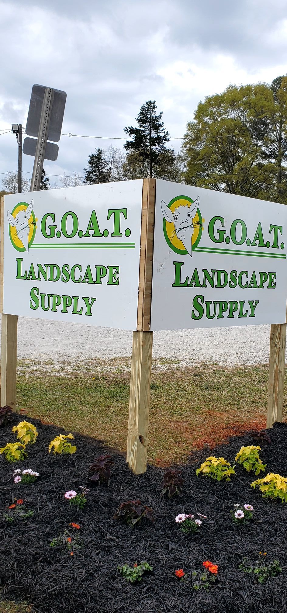 Two signs for G.O.A.T Landscape Supply are sitting next to each other on a wooden post.