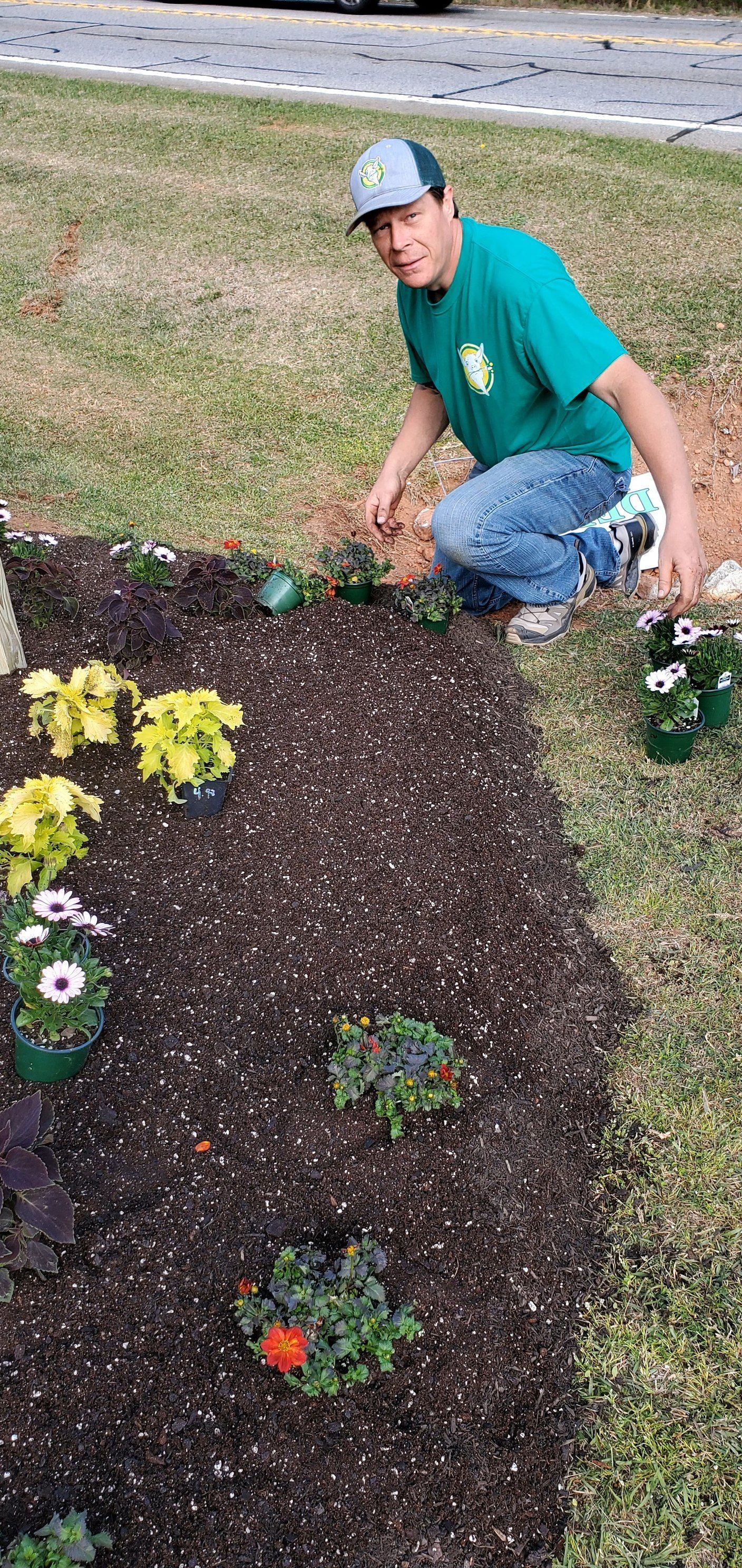 A man is kneeling down in a garden planting flowers.