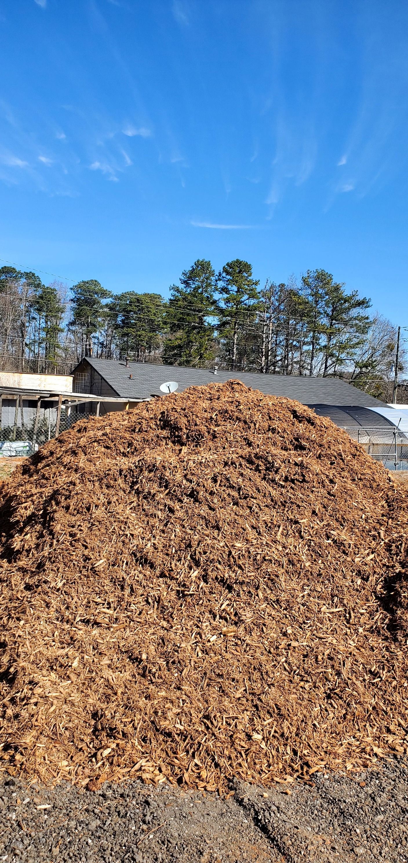 A large pile of wood chips is sitting in front of a house.