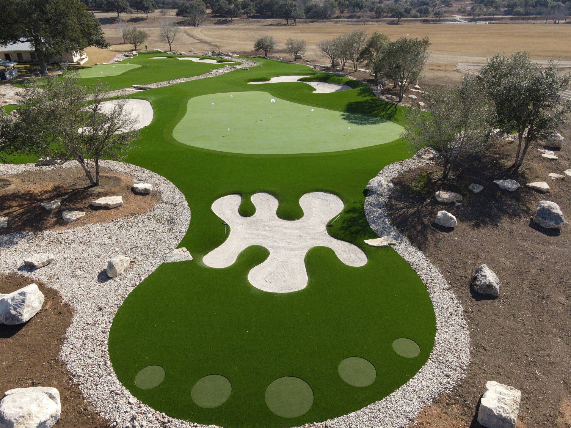 Aerial view of a custom golf green with sand traps, rocks, and trees, outdoors on a sunny day.