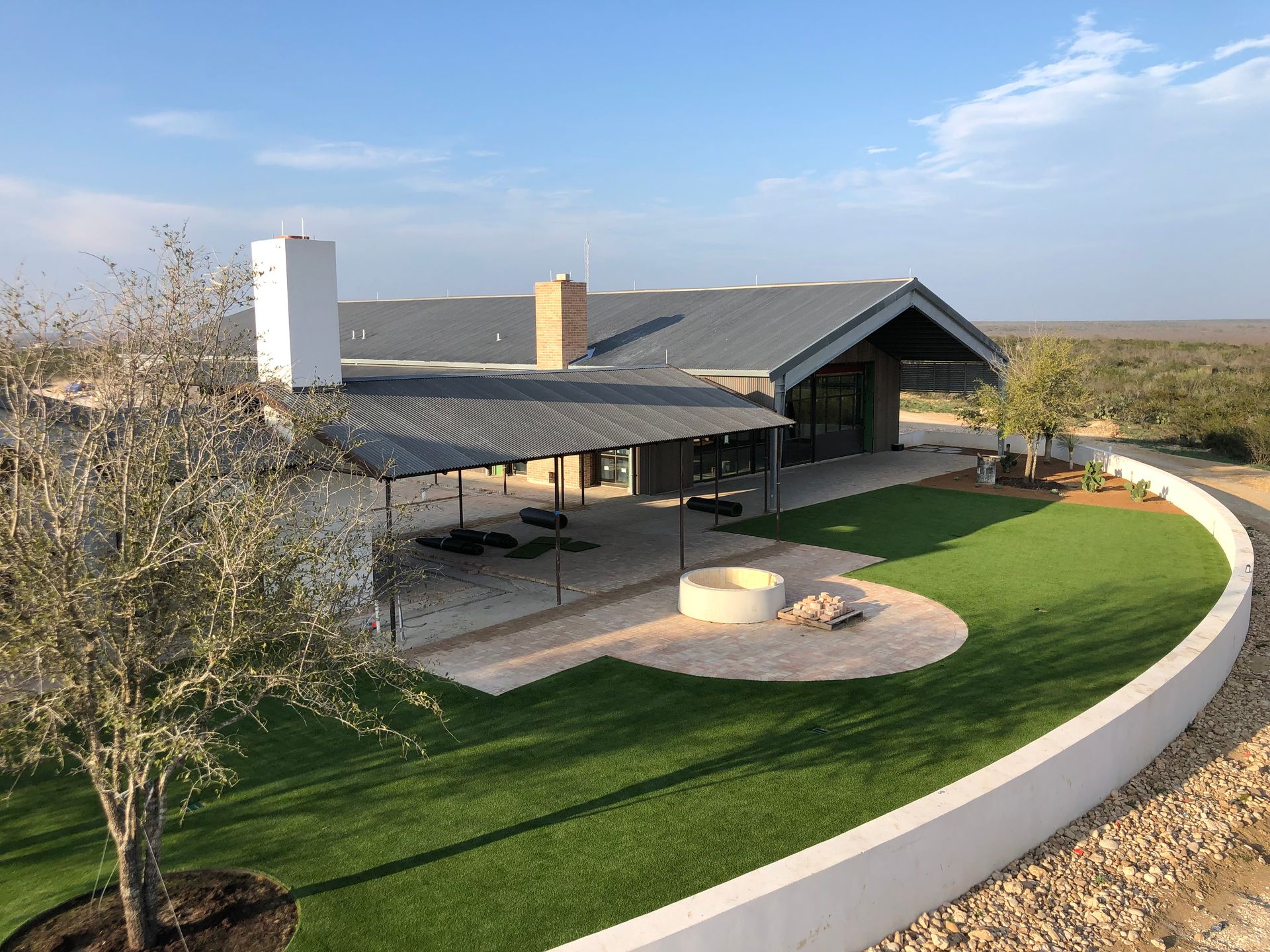 Modern house with a gray roof, outdoor seating area, fire pit, and green lawn against a dry landscape.