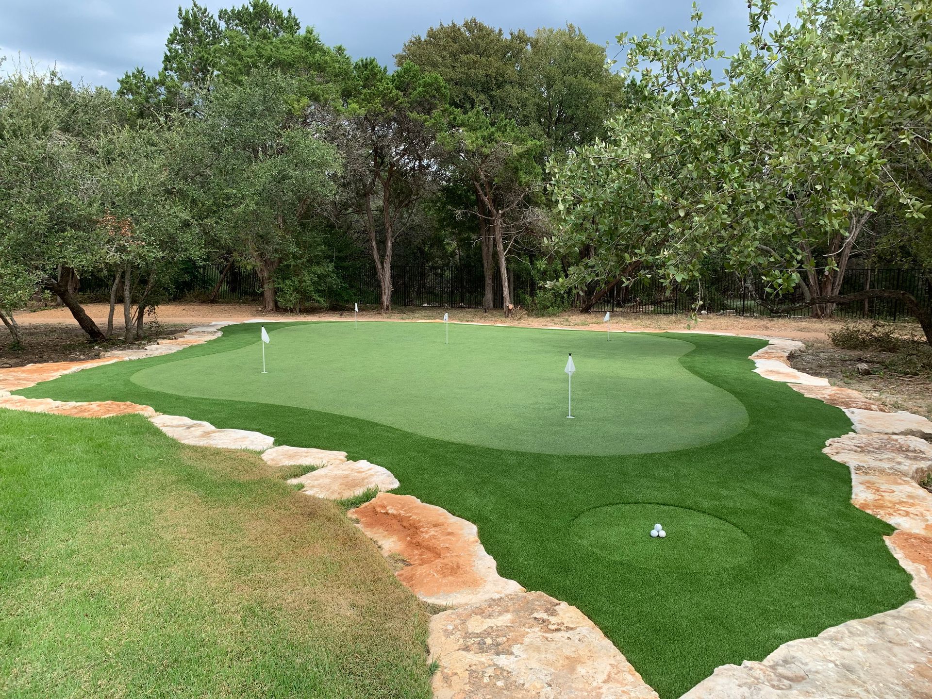 Artificial putting green surrounded by stone and trees; two flags.