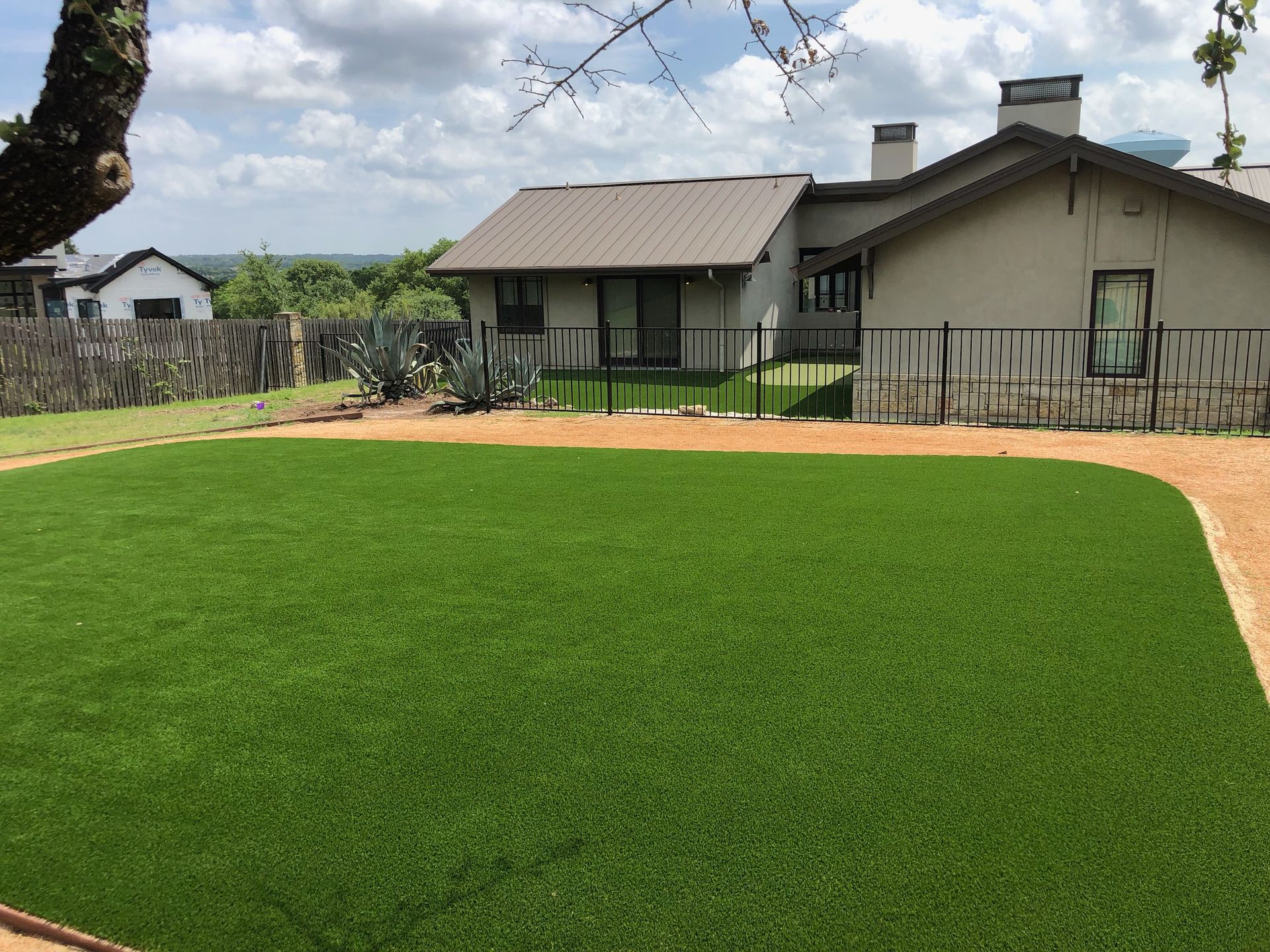 Backyard with green turf and a house with a metal roof, under a cloudy sky.