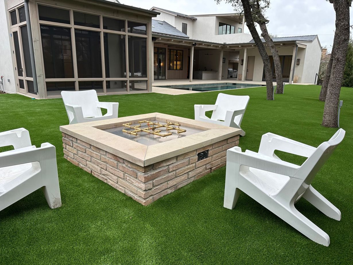 Fire pit surrounded by white chairs on green lawn, house in background.