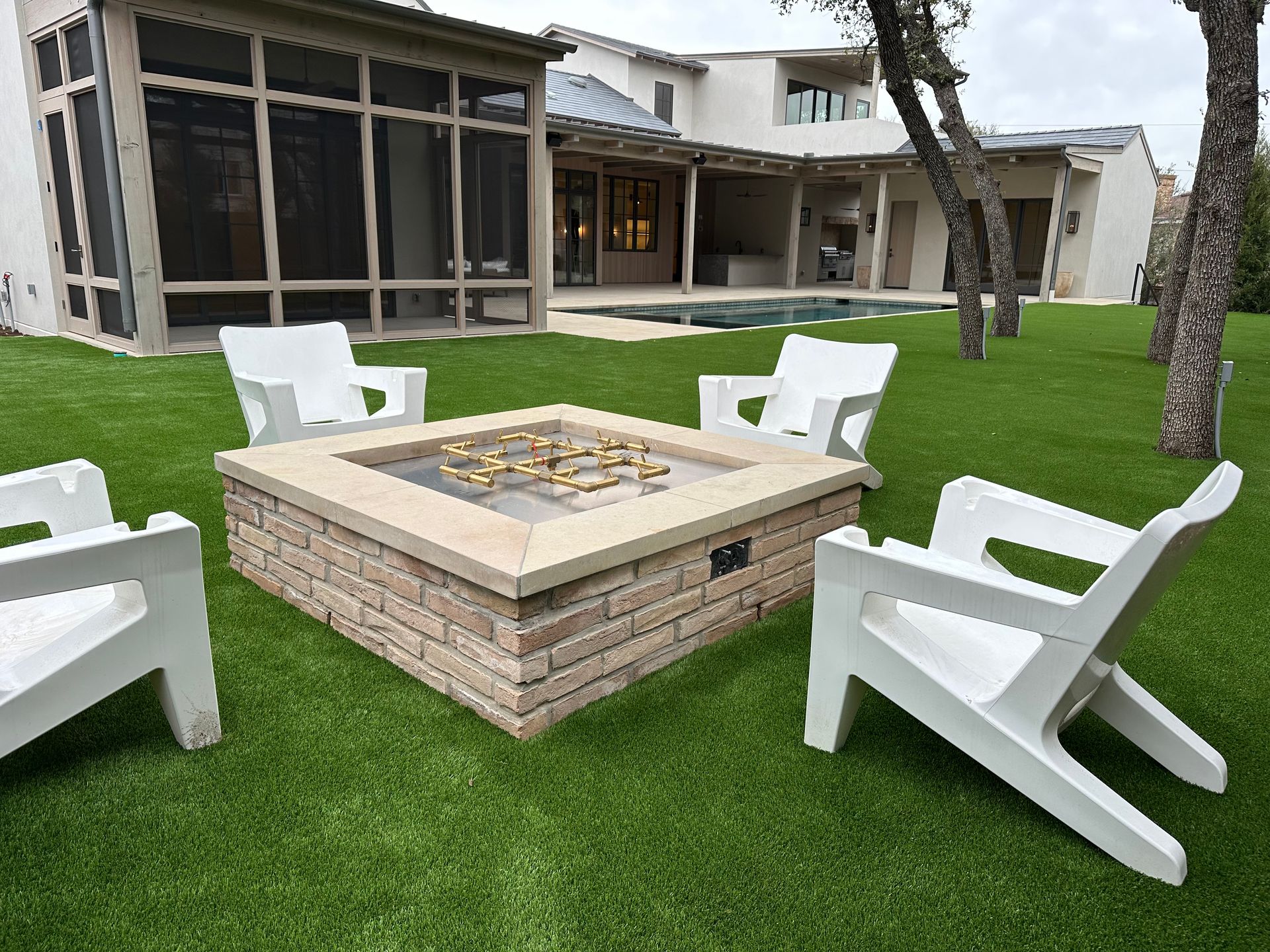 Fire pit surrounded by white chairs on green lawn, house in background.