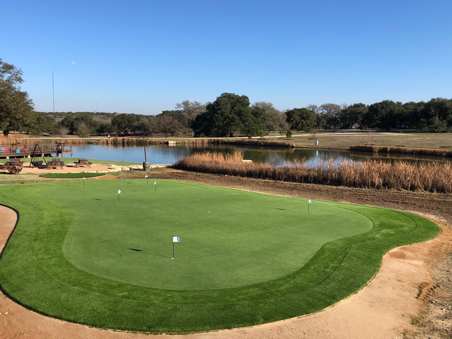 Golf green with flags, pond in the background. Sunny day, clear blue sky.