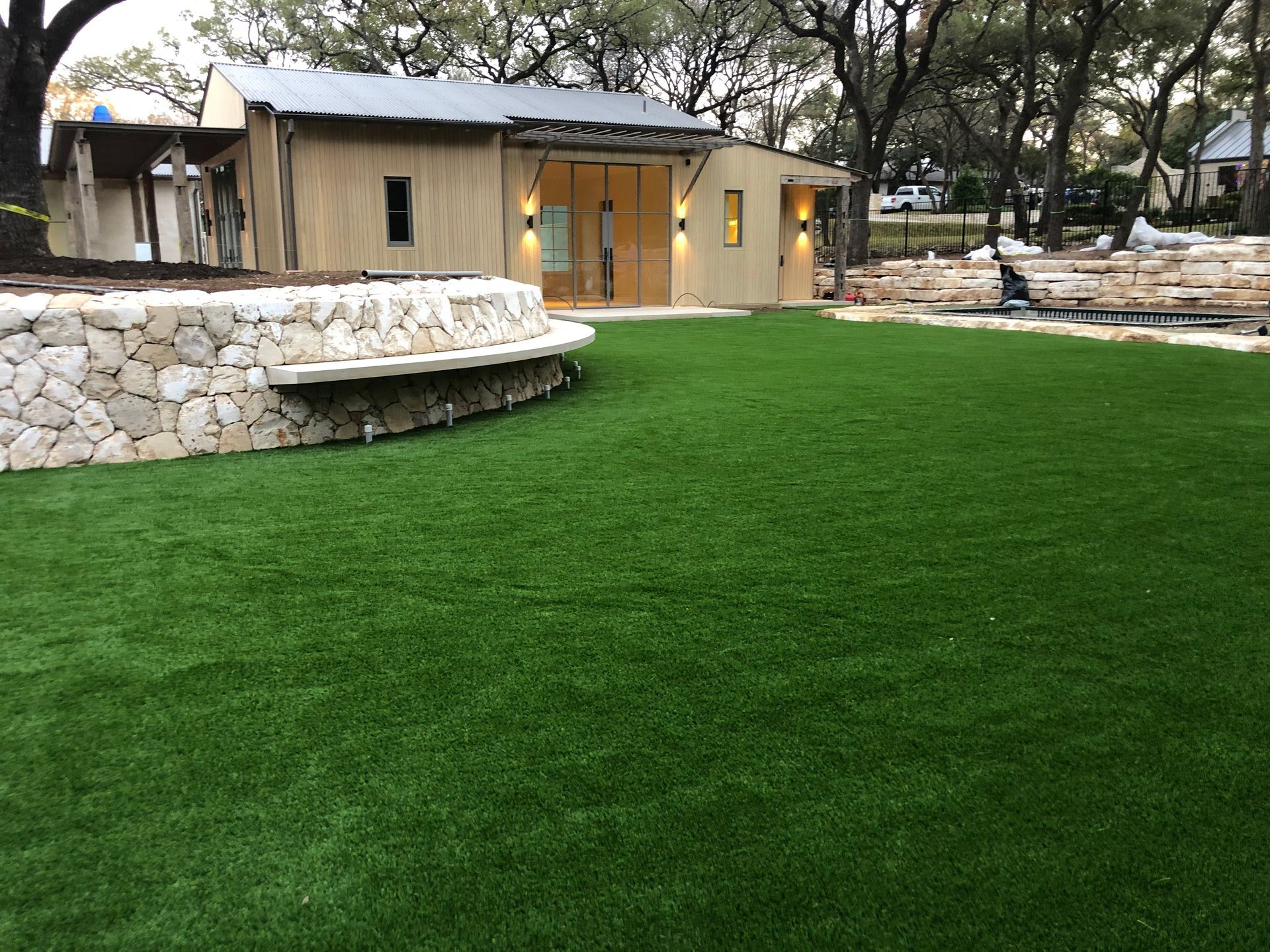 Lush green turf in front of a light brown building with stone retaining wall.