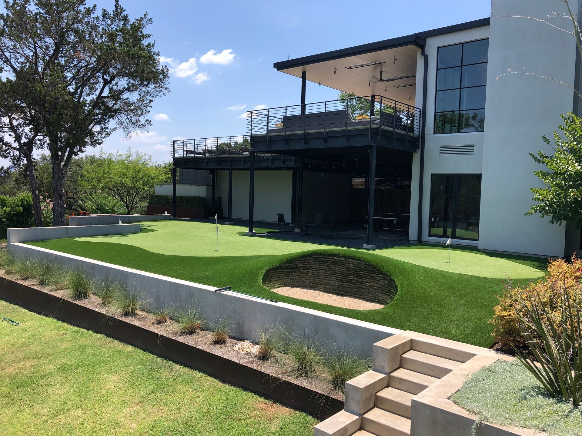 Modern house with a putting green, sand trap, and second-story balcony on a sunny day.