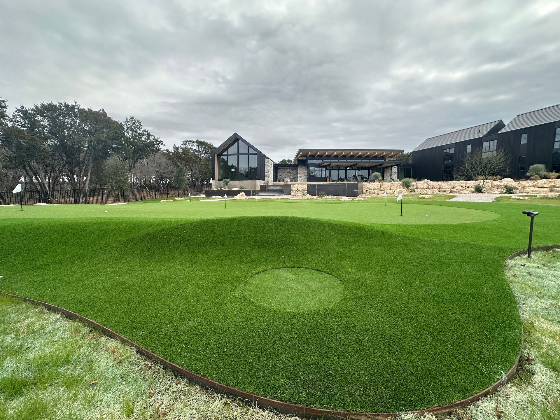 Green artificial turf putting green in front of a modern building under an overcast sky.