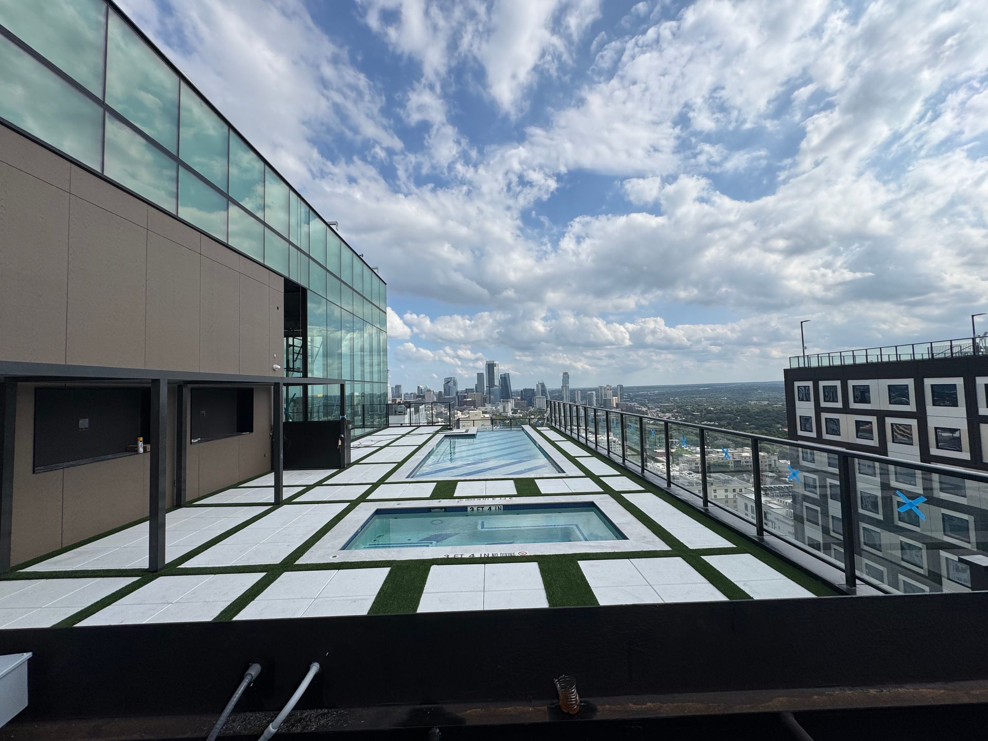 Rooftop pool deck with city skyline view, blue sky, and white clouds.