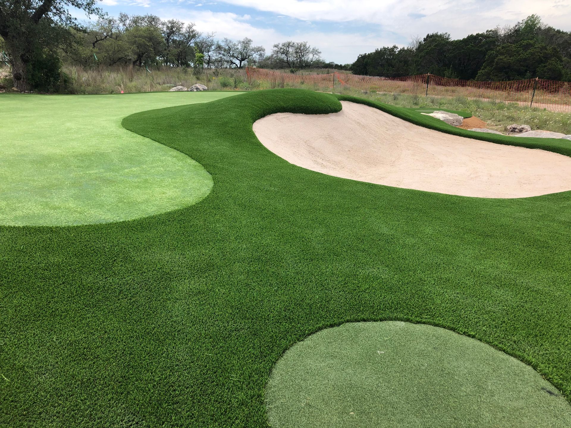 Green golf course with sand trap and patches of different grasses.