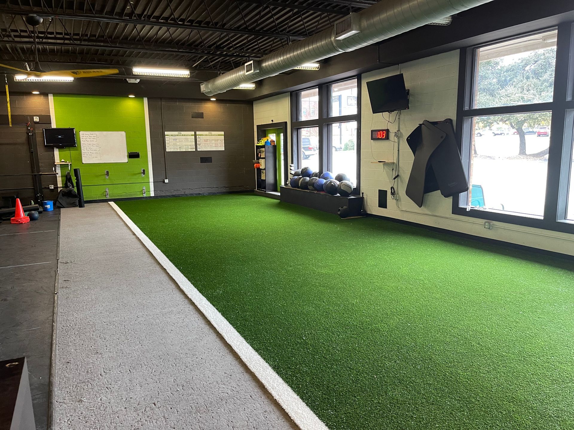 Gym interior with turf floor, weights, and large windows.