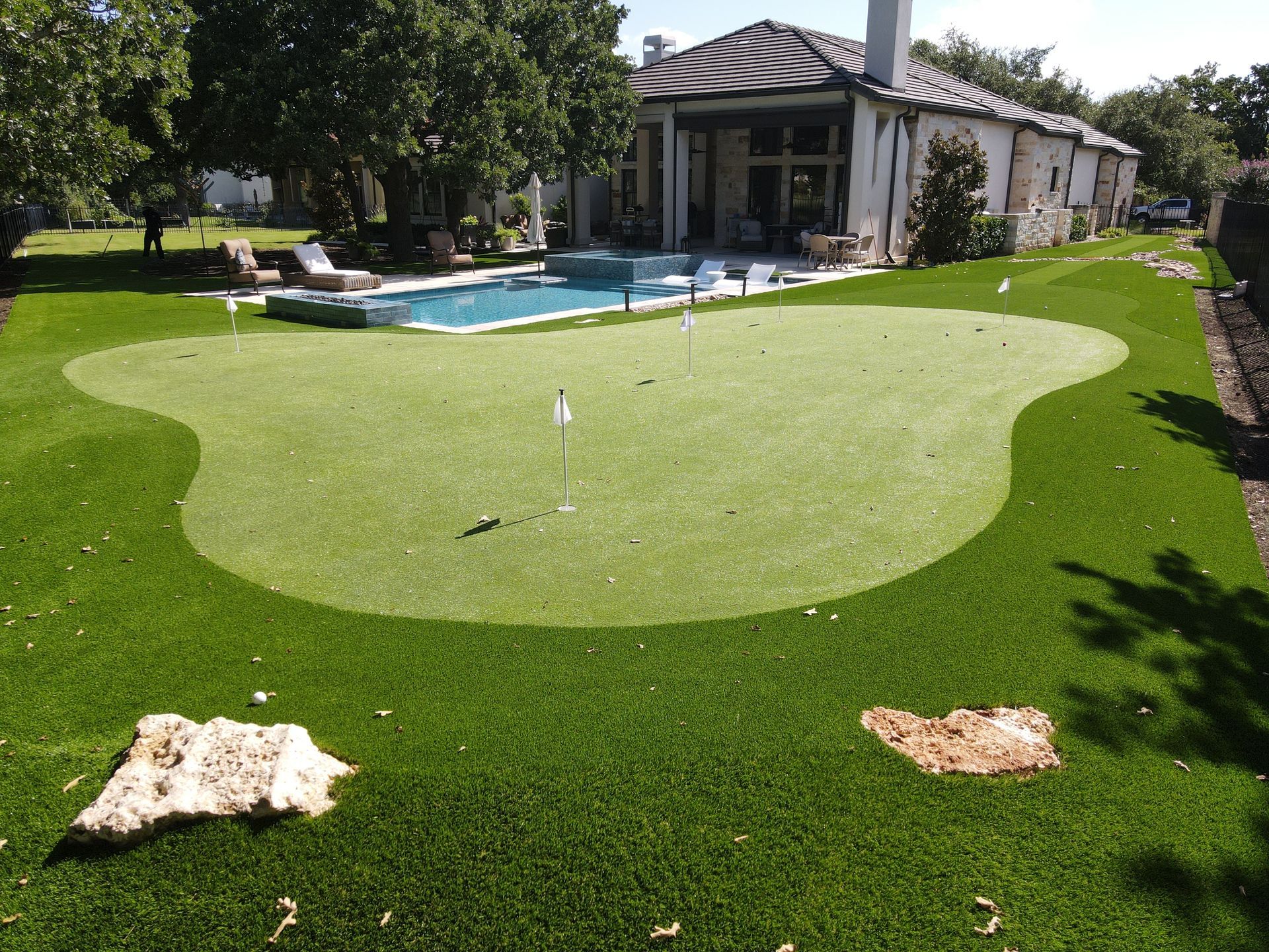 Backyard putting green with a pool and house in the background. Green artificial turf.
