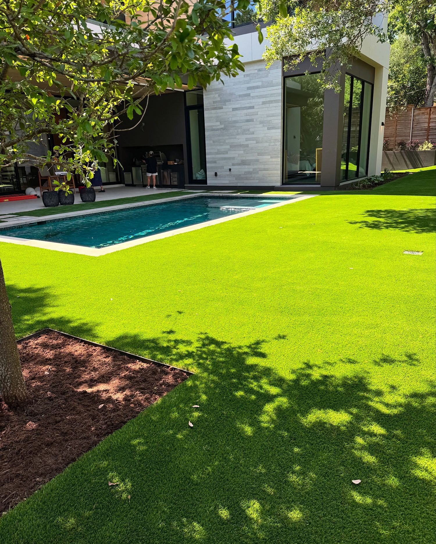 Modern home with pool, lush green lawn, trees, and bright sunlight.