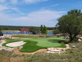 Golf green with sand trap, wooden fence, and lake in background. Sunny day.