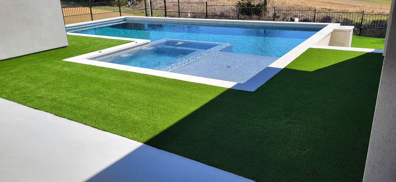 A swimming pool with artificial green grass surrounding it. Blue water in the pool under a sunny sky.