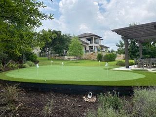A backyard putting green with flags, next to a home and a pergola.