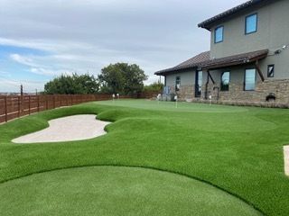 Backyard putting green with a sand trap, next to a two-story house.