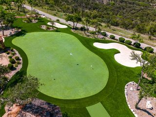 Aerial view of a golf putting green with sand traps, surrounded by green turf and trees.
