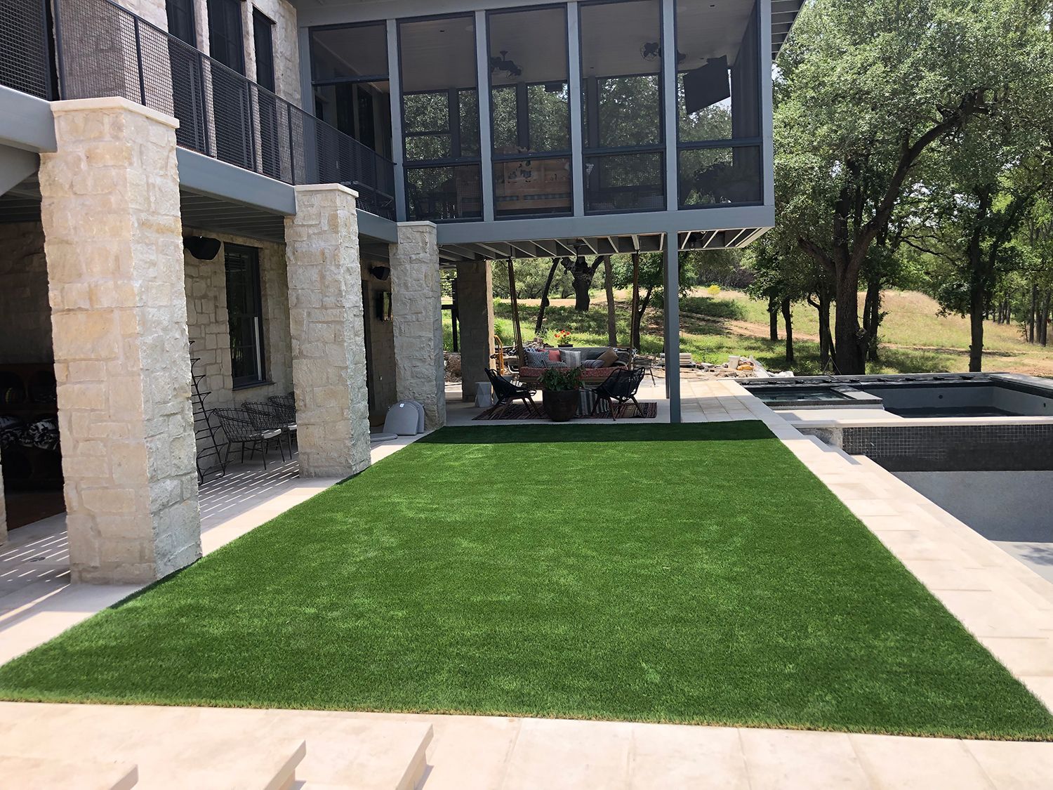 Green artificial turf next to a house with a porch and pool.