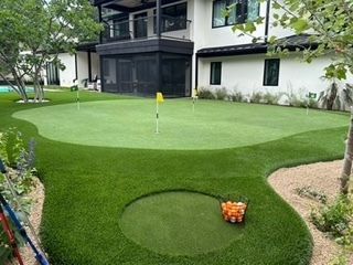 Backyard putting green with multiple holes, golf balls, and a house in the background.