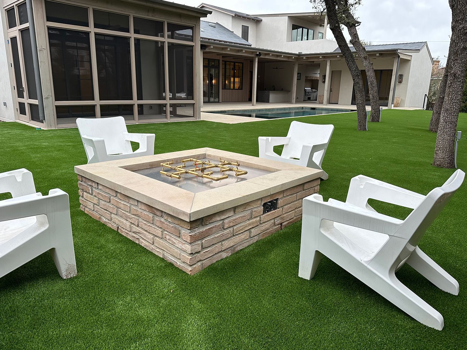 Fire pit with white chairs on green lawn, house in background.
