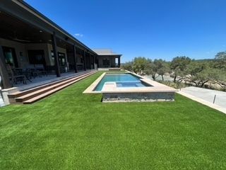 A home with a rectangular pool and a lush green lawn. The sky is bright blue.