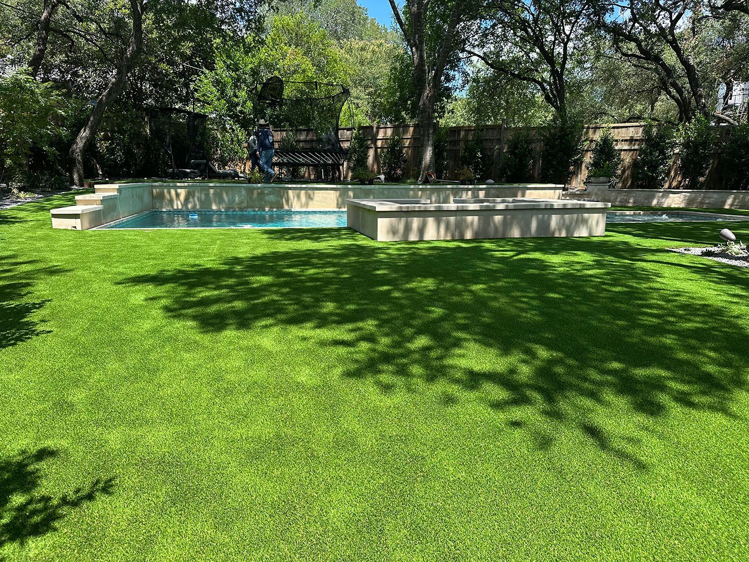 Lush green lawn with a rectangular pool, surrounded by stone structures and trees.