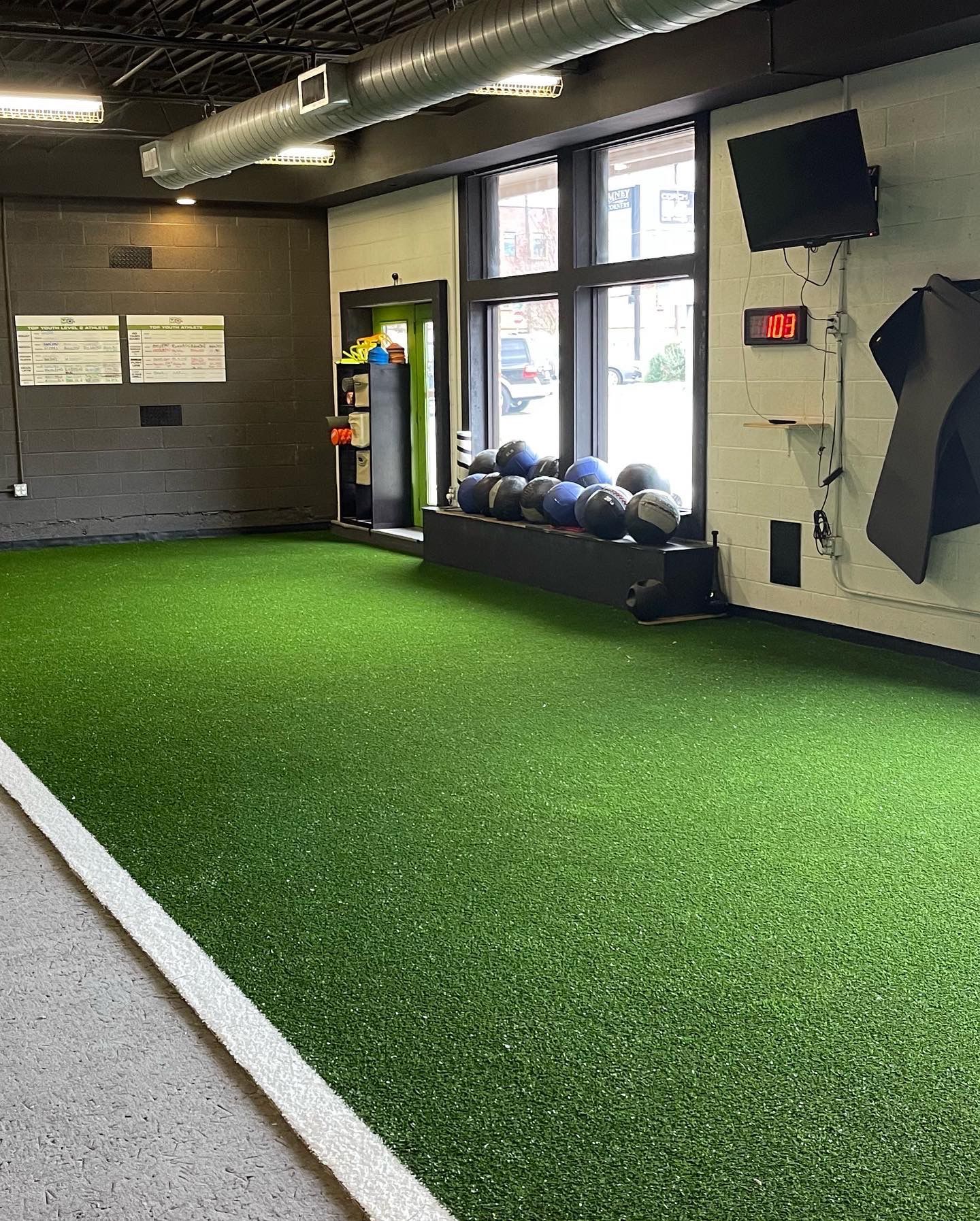 Indoor gym space with green turf floor, exercise balls, and a window.