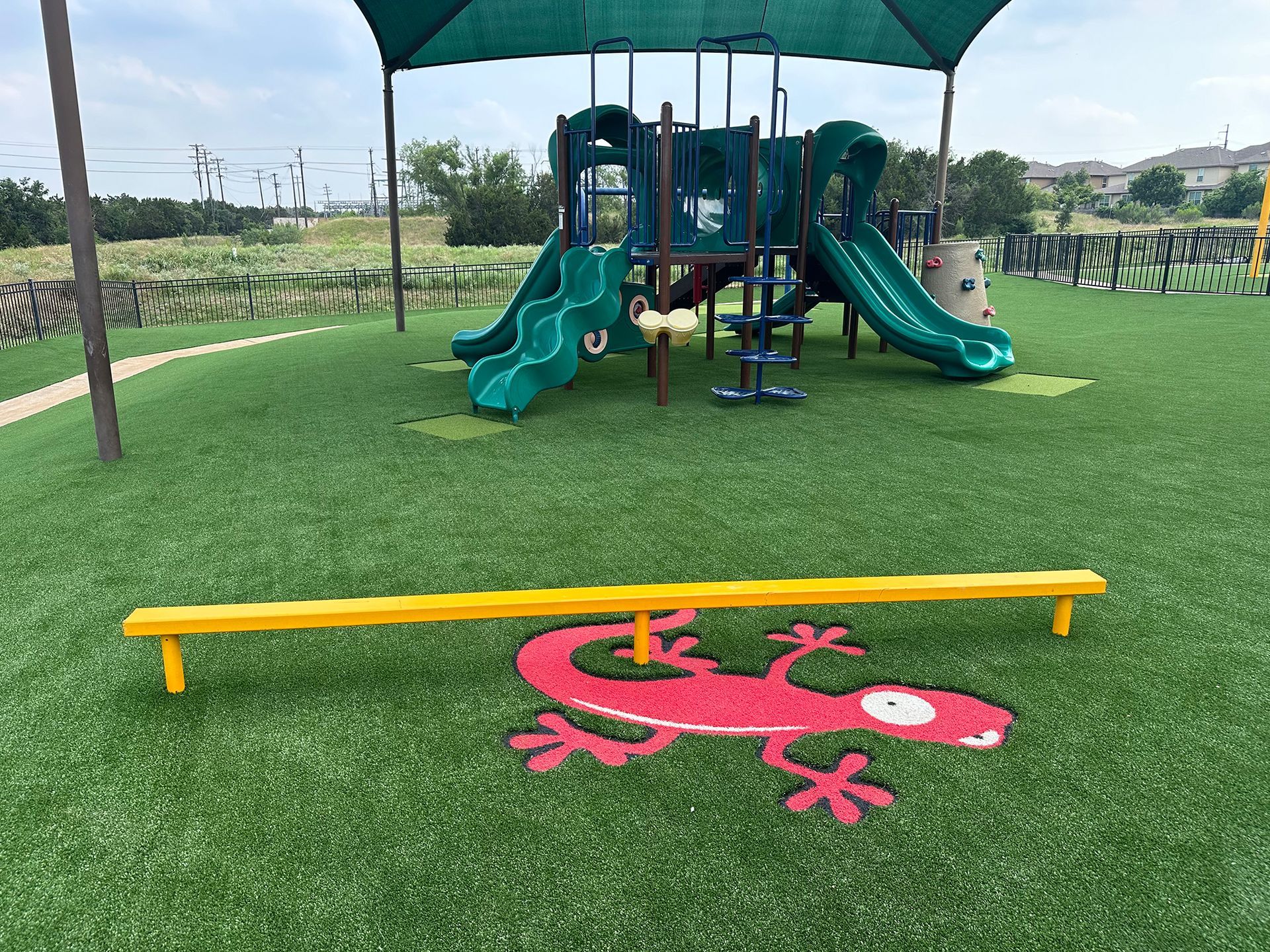 Playground with green slides, a yellow balance beam, and a red lizard graphic on green turf.