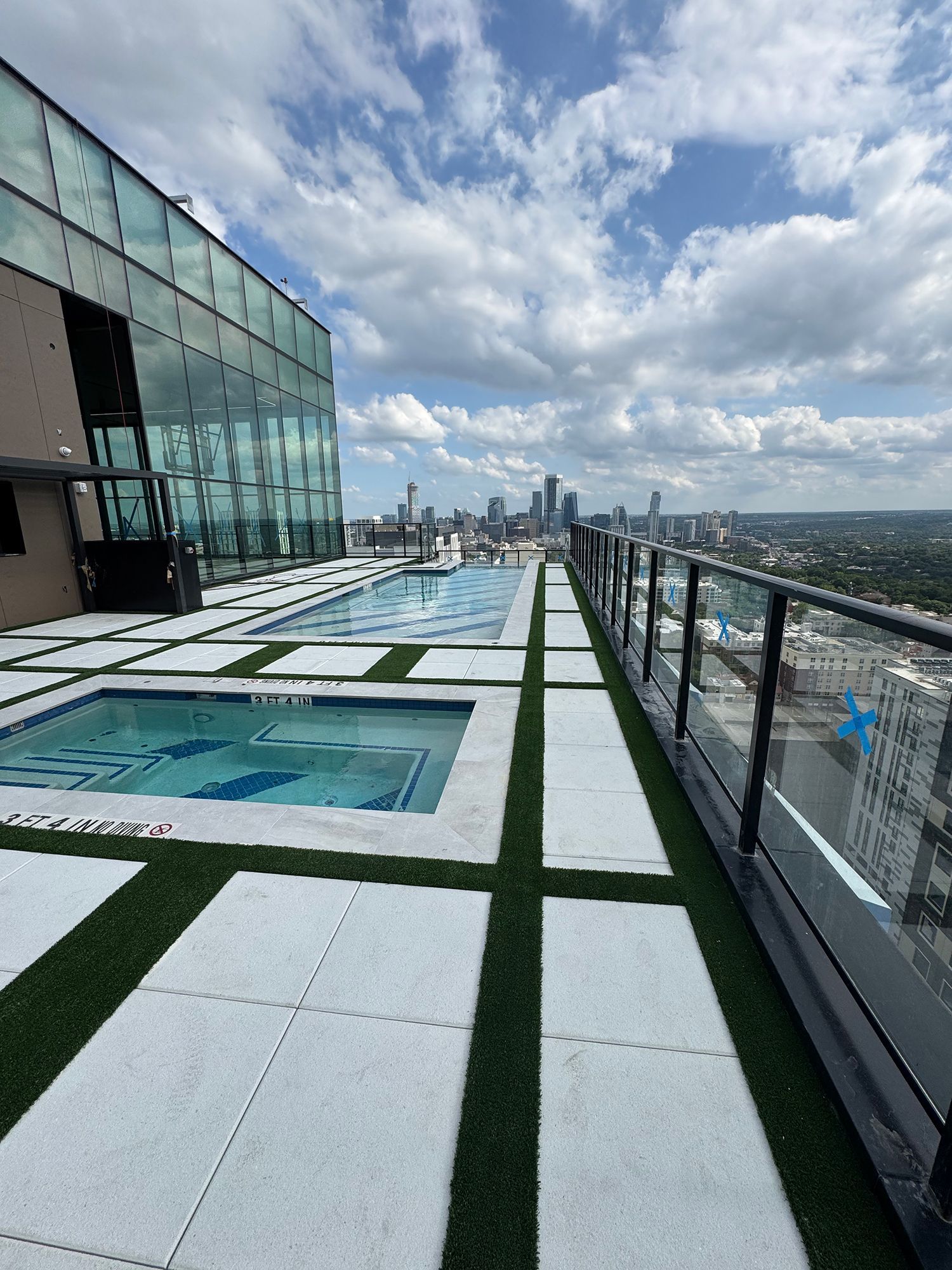 Rooftop pool and deck with city skyline view under a partly cloudy sky.