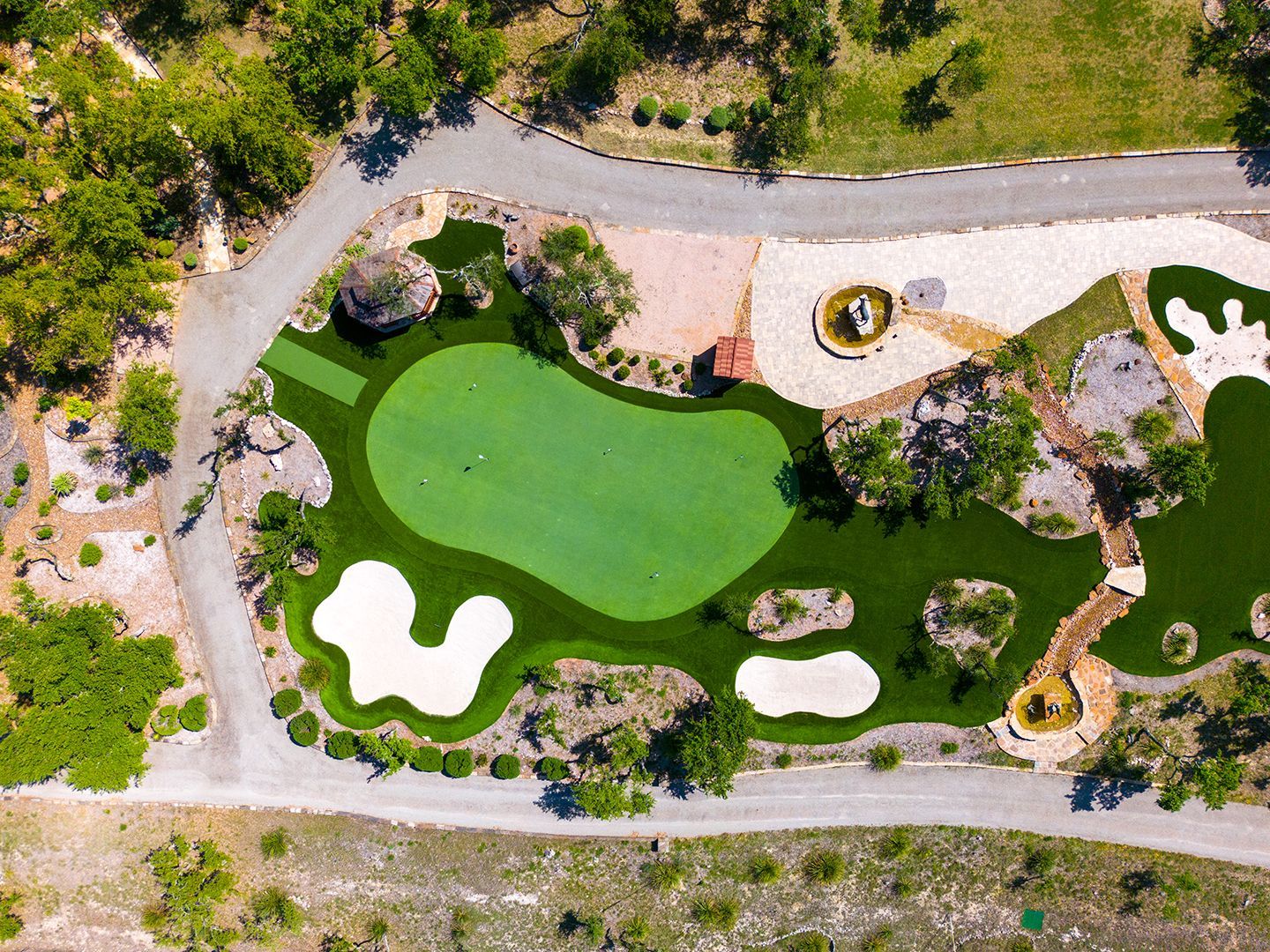 Aerial view of a custom putting green with sand traps, surrounded by artificial turf, rock features, and pathways.