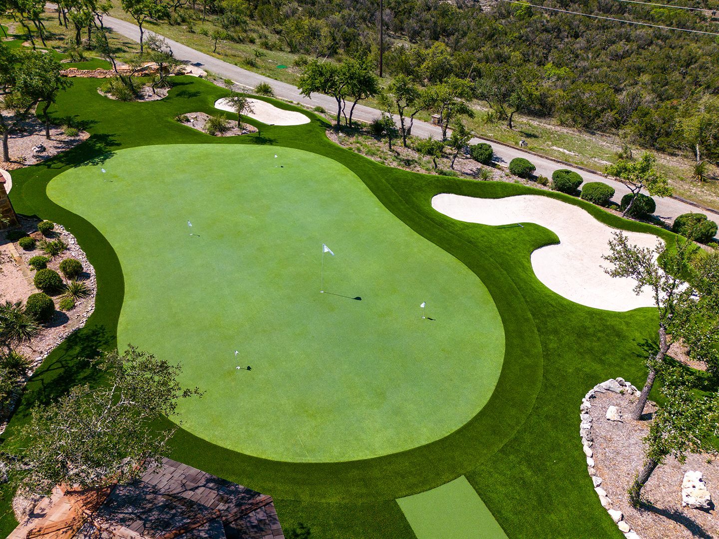 Aerial view of a custom putting green surrounded by landscaping, sand traps, and pathways, in an outdoor setting.