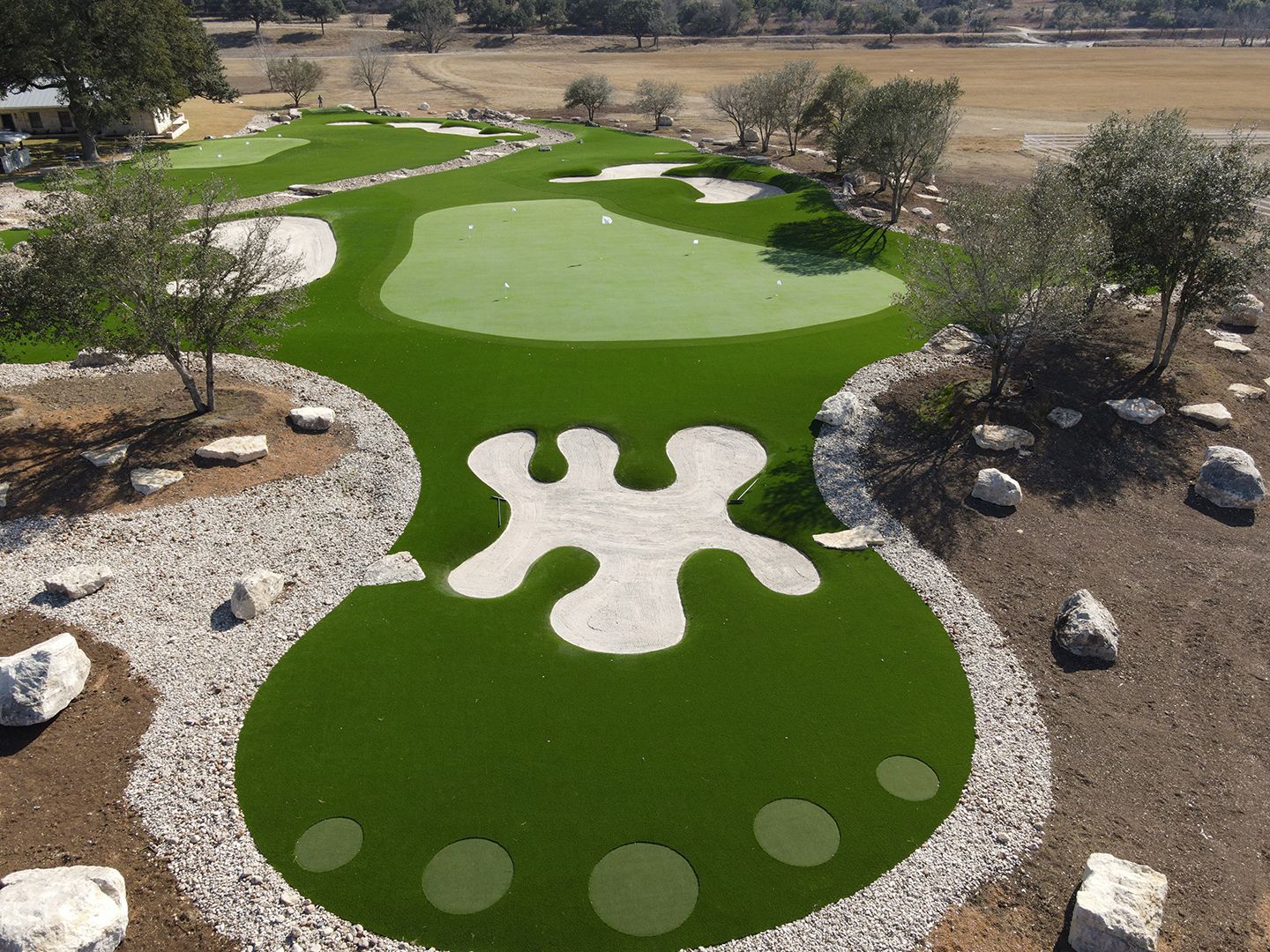Aerial view of a custom golf putting green with a unique sand trap design, surrounded by rocks and trees.