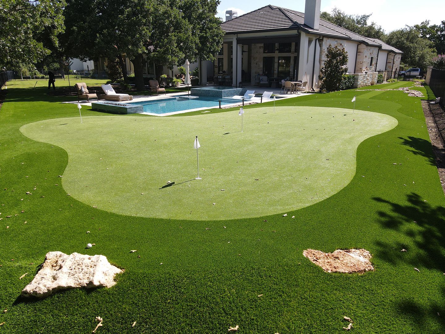 Backyard with putting green, pool, and house. Green lawn with golf flags.