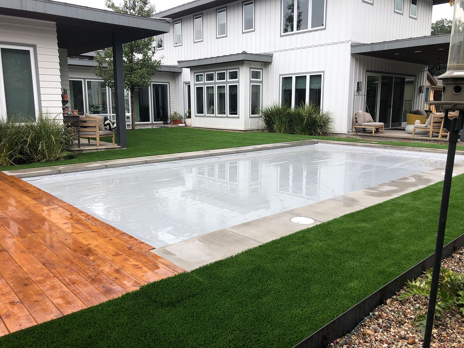Pool covered in front of a white two-story house with green turf and a wooden deck.