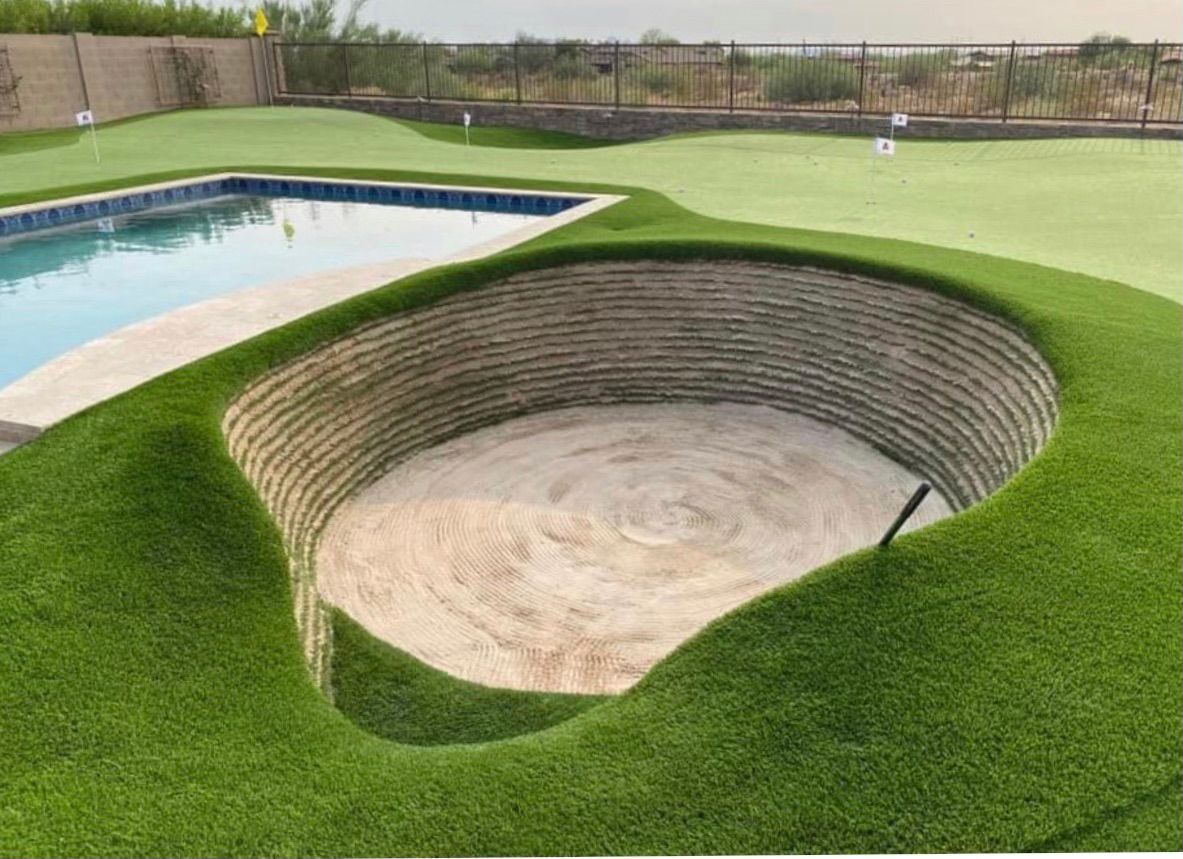 Backyard with pool and putting green featuring an excavated sand area surrounded by tiered walls and artificial turf.