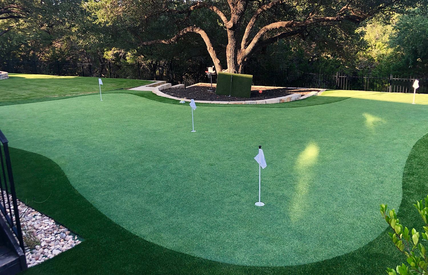 A backyard putting green with multiple flags. Lush green turf, surrounded by trees.