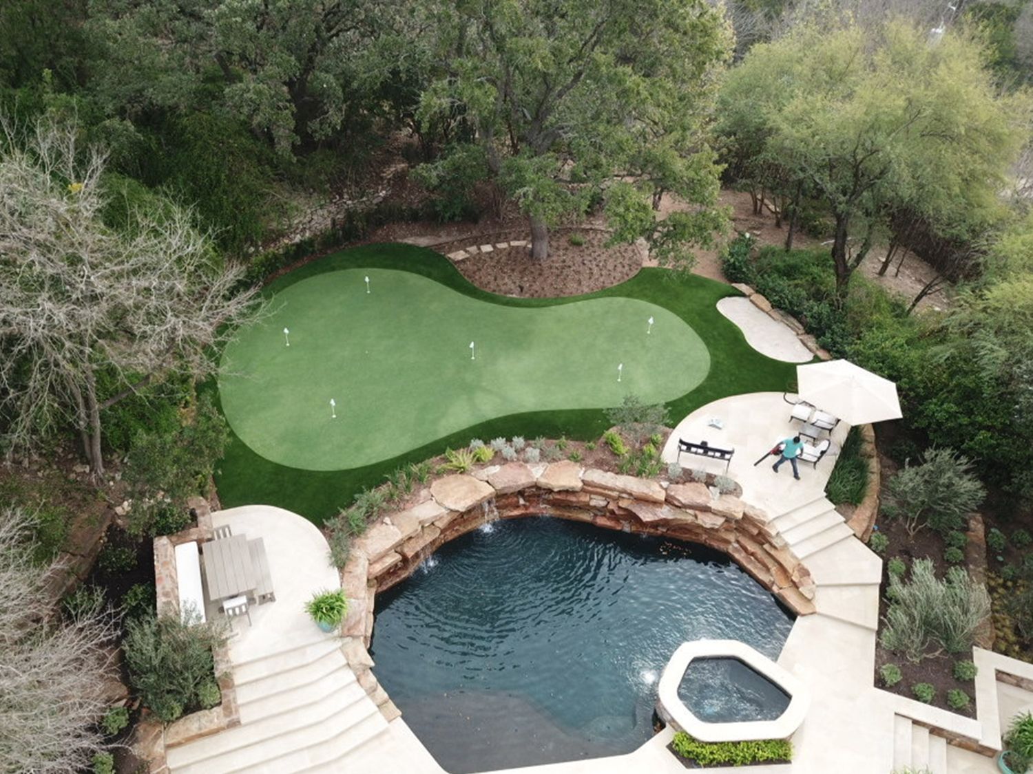 Golf green and swimming pool in a lush backyard setting. Features include a putting green, waterfall, and patio seating.