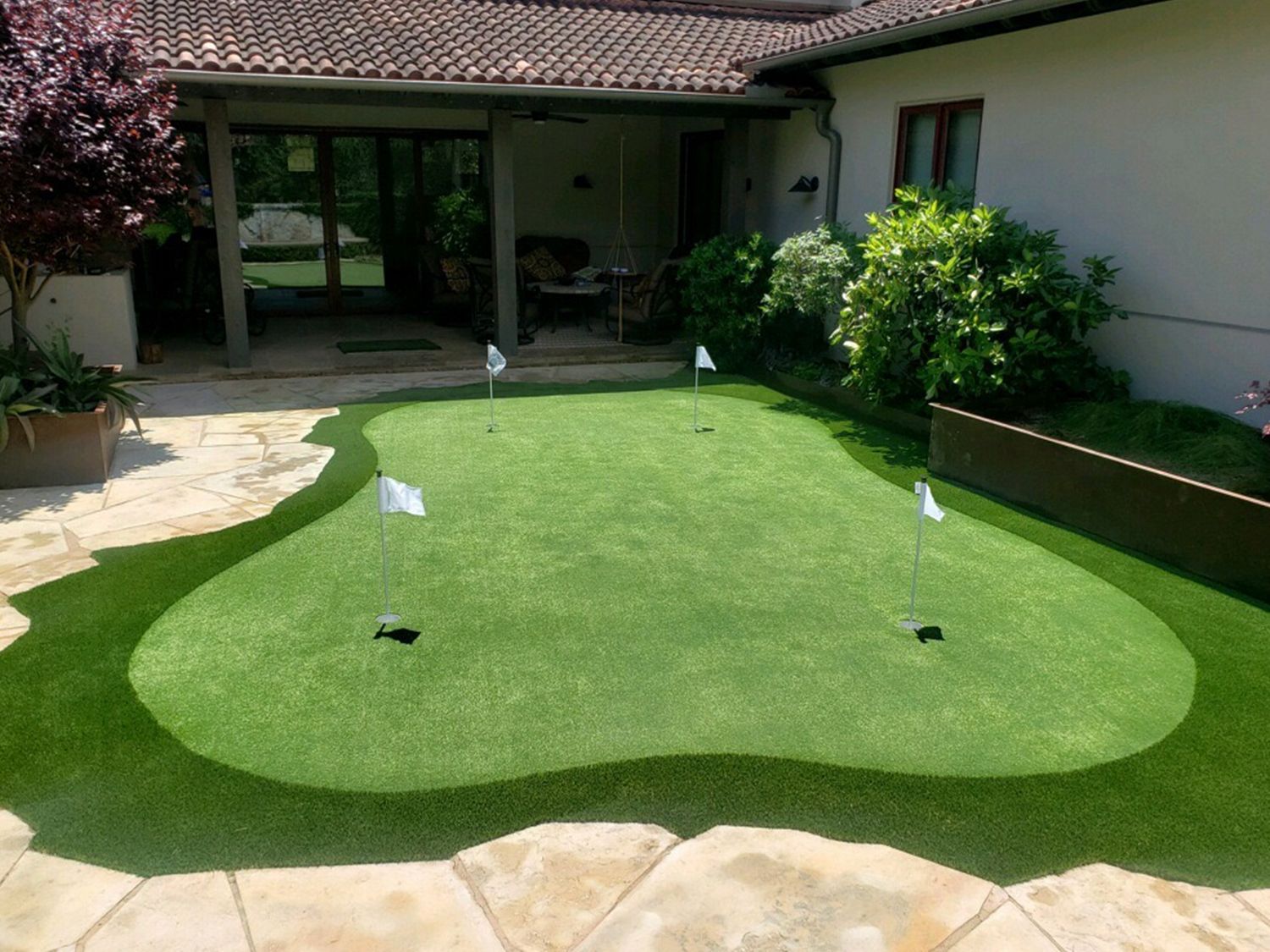 Artificial grass putting green with flags in a backyard.
