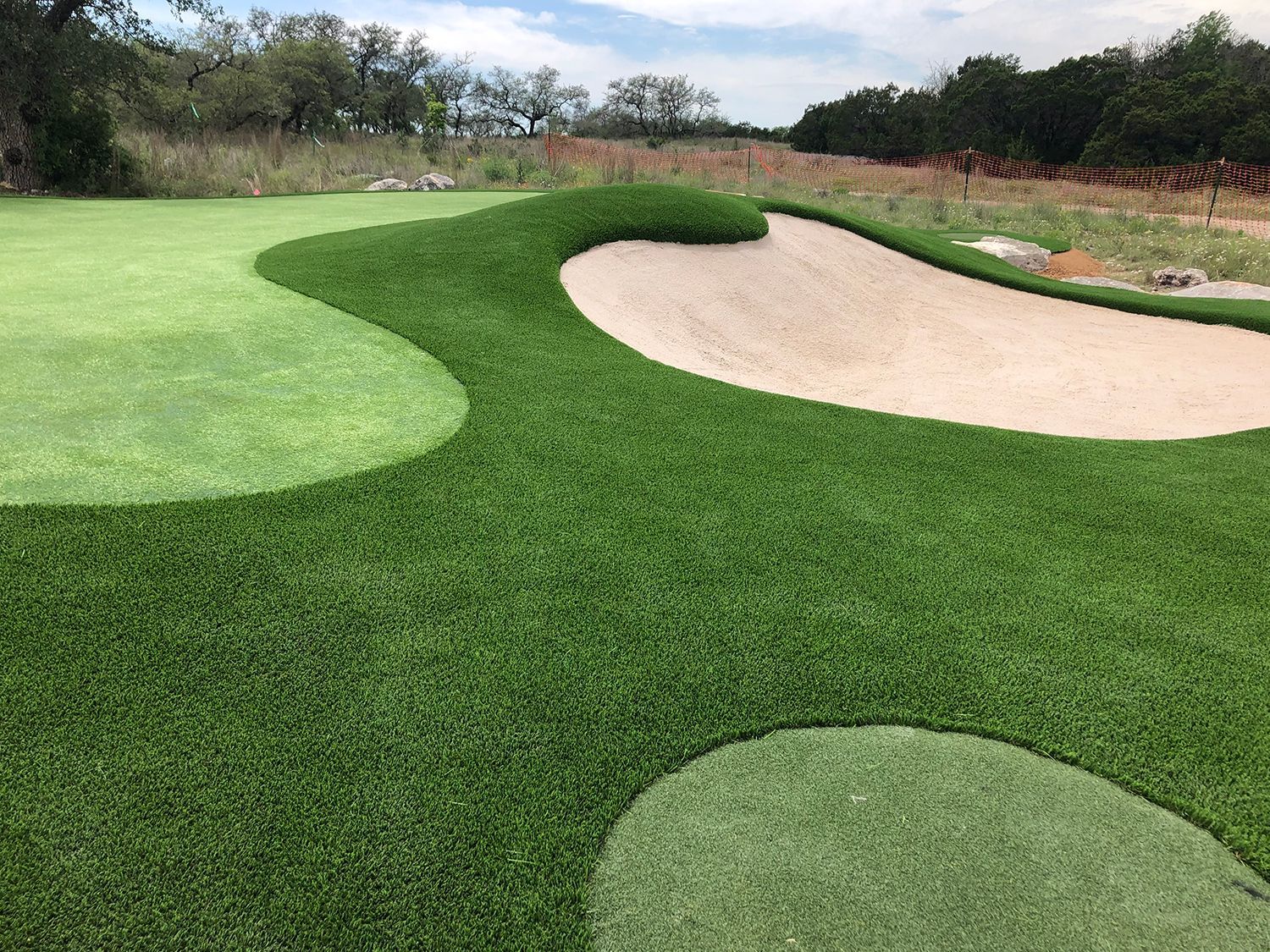 Golf green with a sand trap and lush artificial turf.