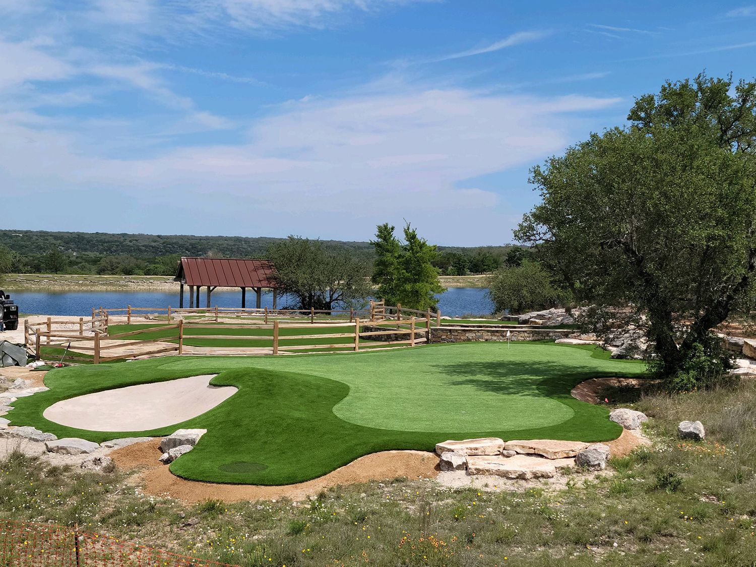 Golf putting green with sand trap, scenic view of lake and wooden pavilion. Sunny day.